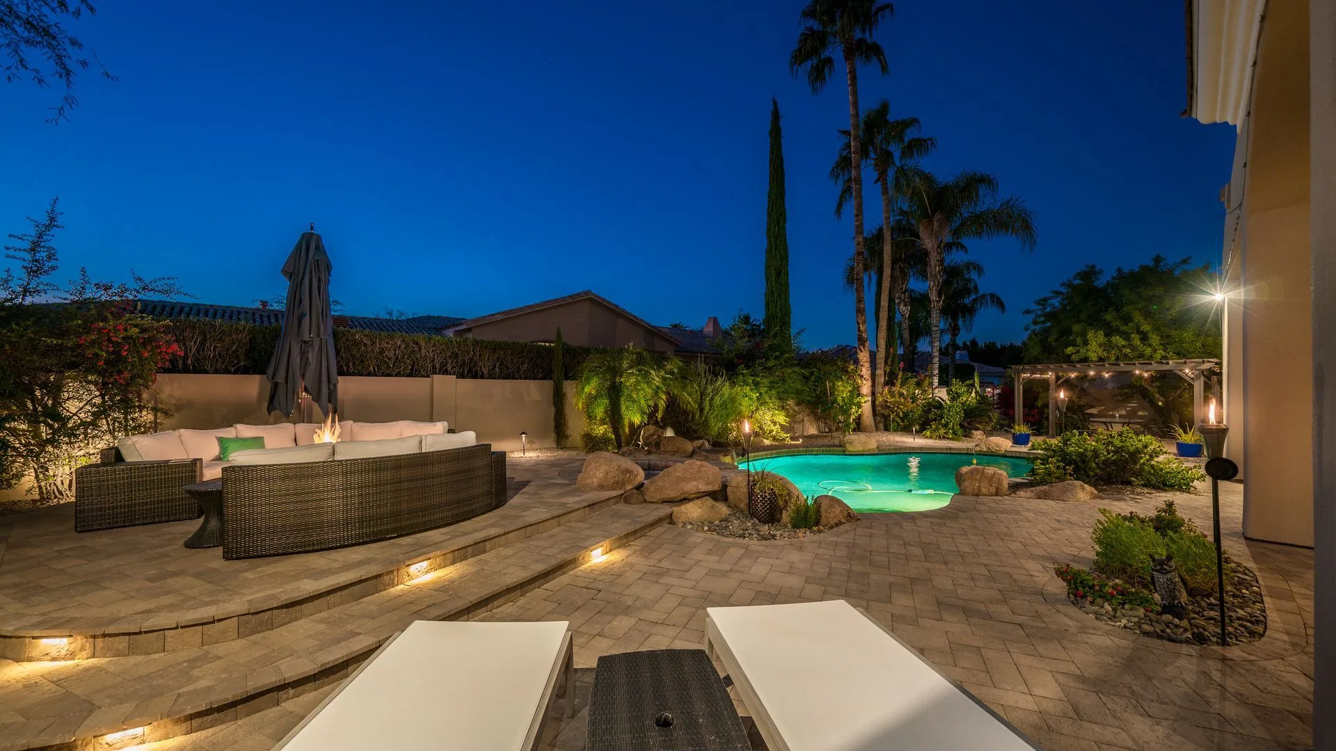 Paver patio with a fire feature and lit pool at dusk by Diamond Cut Landscape