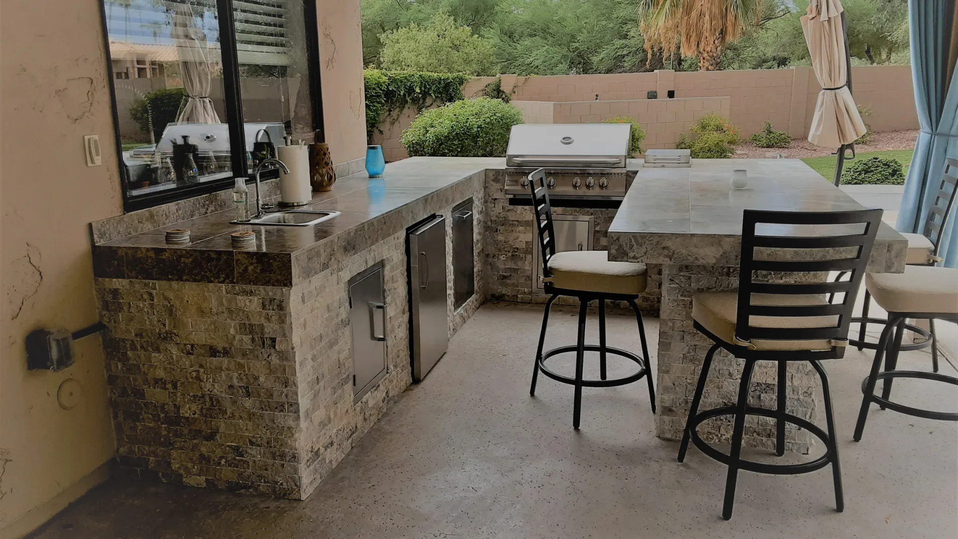 Full L-shaped outdoor kitchen with grill, fridge, sink, and raised bar seating