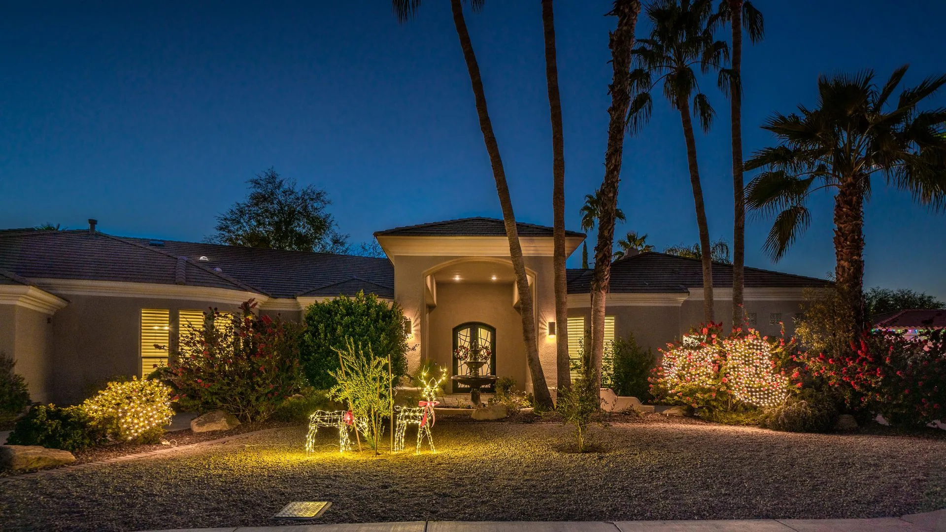 Lit front-yard design at dusk with palms, planting, and pathway lighting