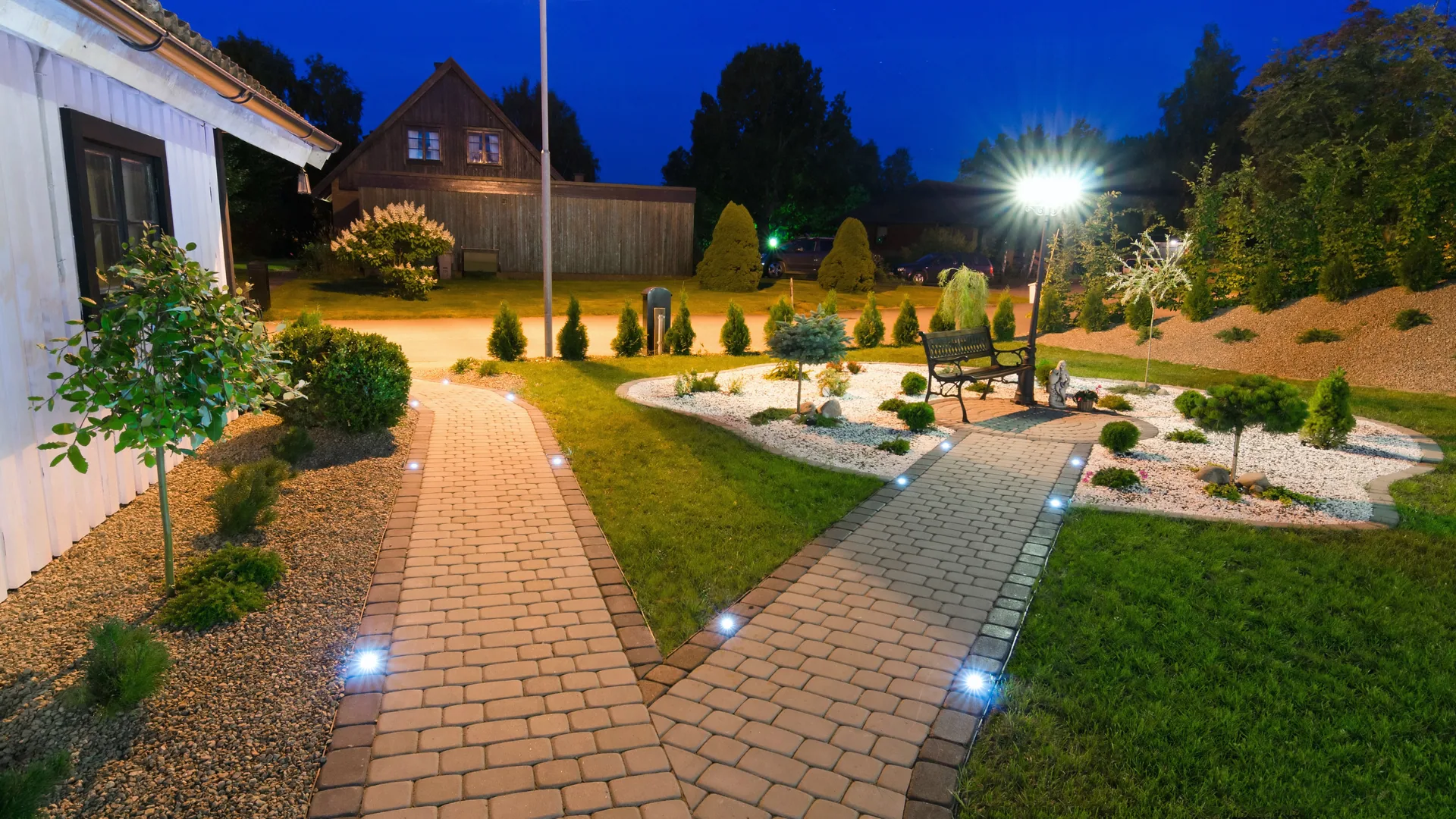 Backyard at night with paver paths lit by low-voltage path lights and an uplit tree