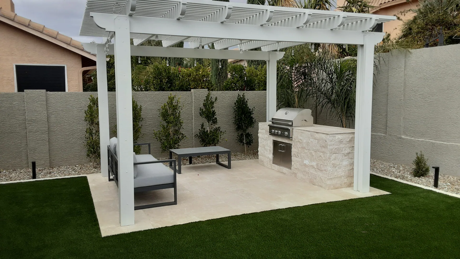 White pergola over a patio with seating and a built-in grill