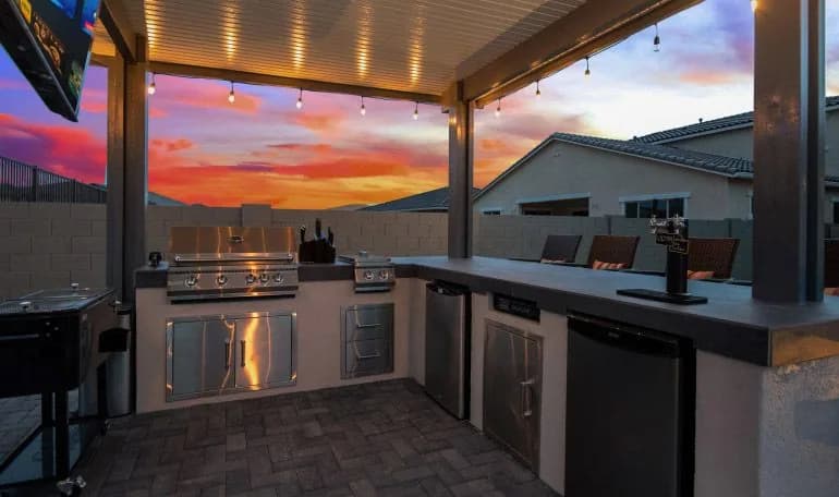 Custom outdoor kitchen with grill island under string lights at sunset