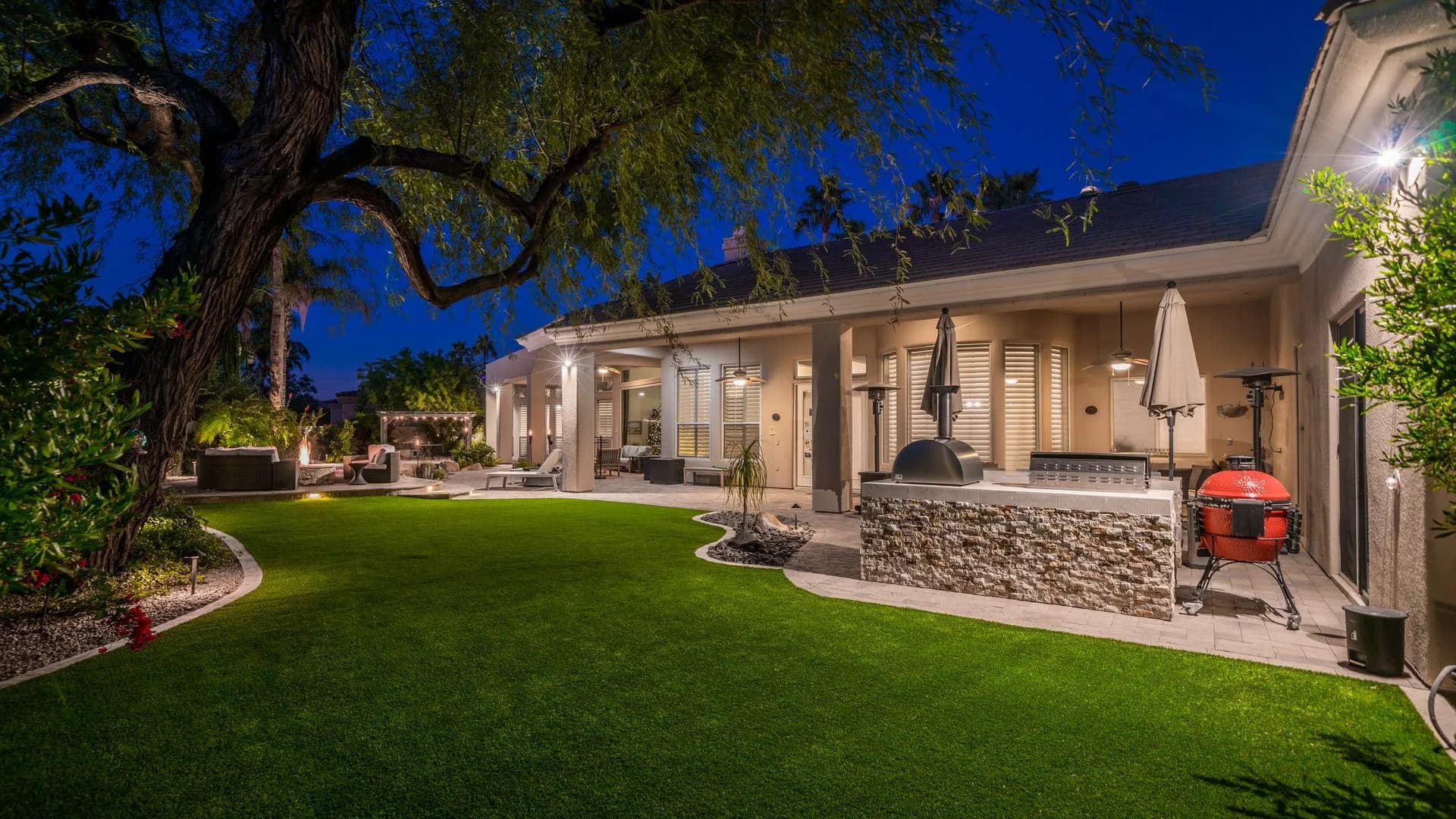 Lush green lawn with mature trees and outdoor lighting at dusk