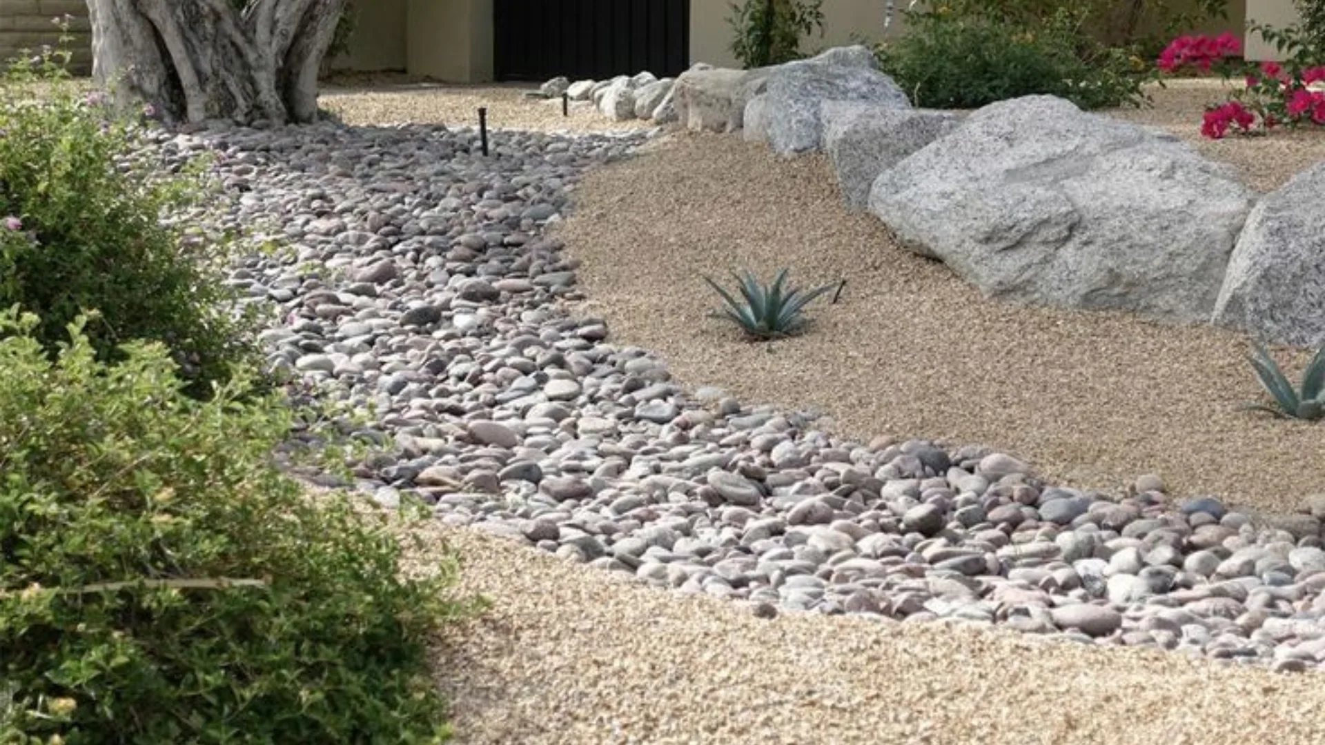Dry creek bed of smooth river cobble winding through decomposed granite