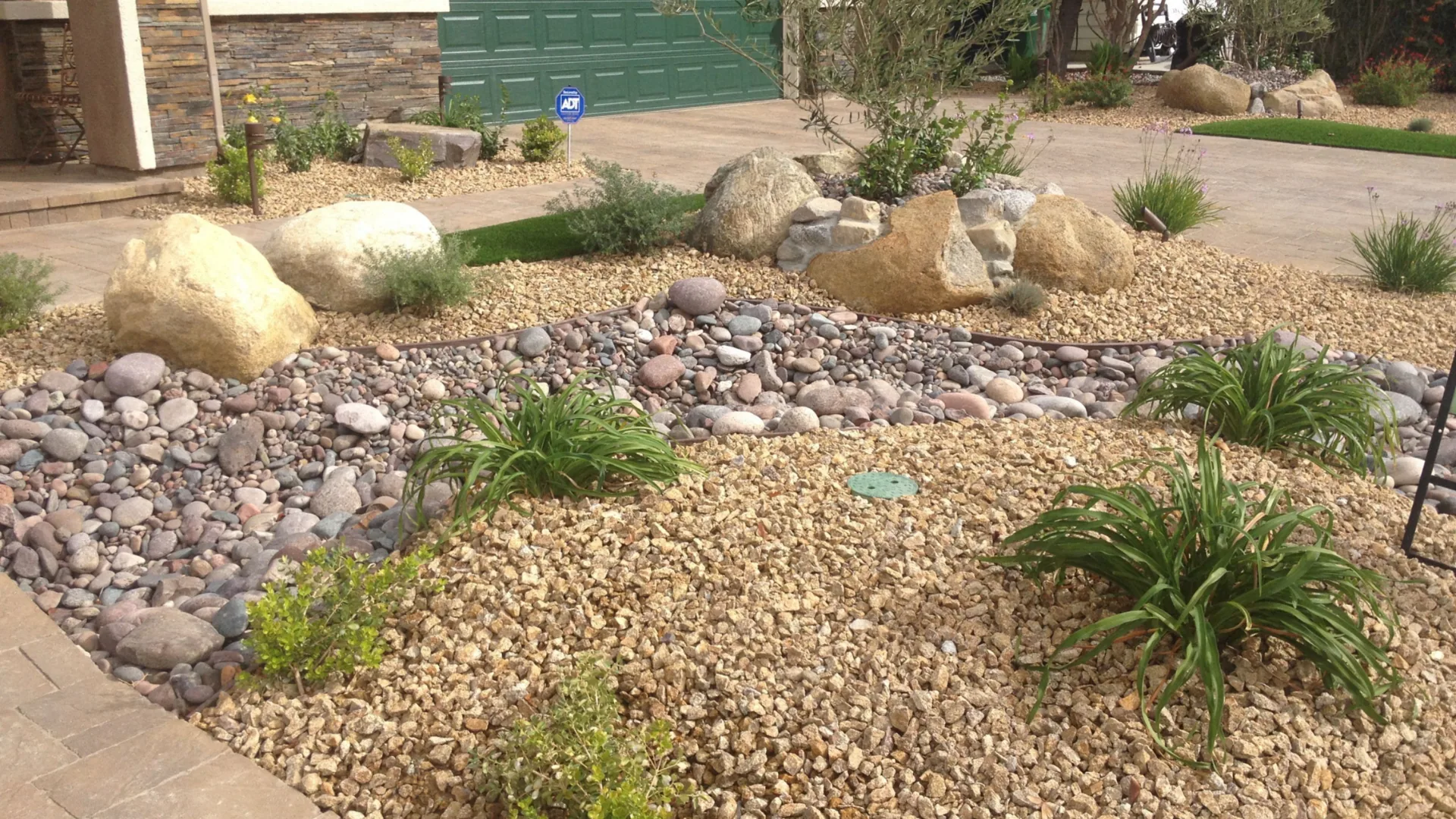 Front-yard rock installation with decorative gravel, a dry creek bed, and boulders